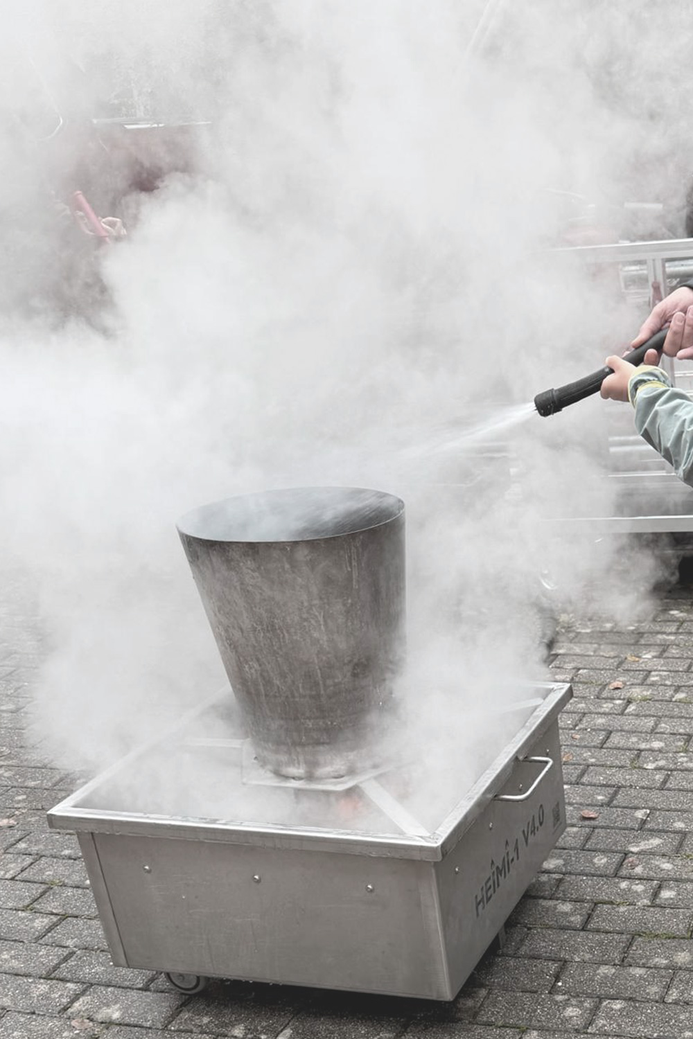 Feuersimulator für Muelleimerbrand auf den das Strahlrohr eines Feuerlöschers gerichtet ist