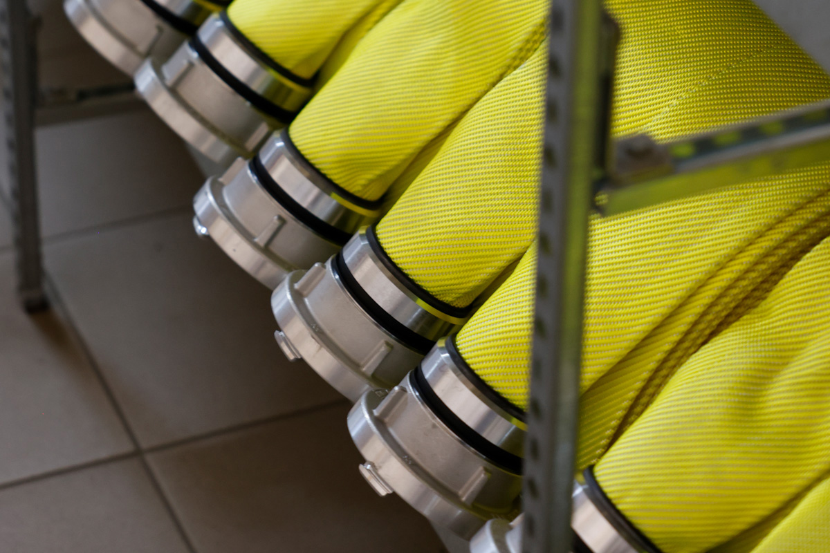 Feuerwehrschläuche in der Farbe Neongelb liegen gerollt in Reihe in einem Schlauchregal.