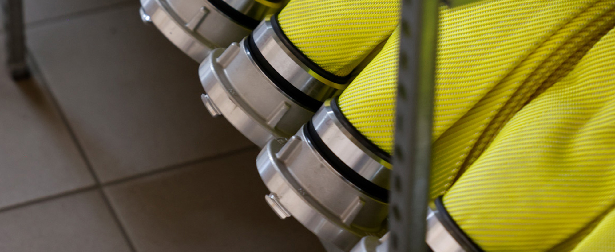 Feuerwehrschläuche in der Farbe Neongelb liegen gerollt in Reihe in einem Schlauchregal.